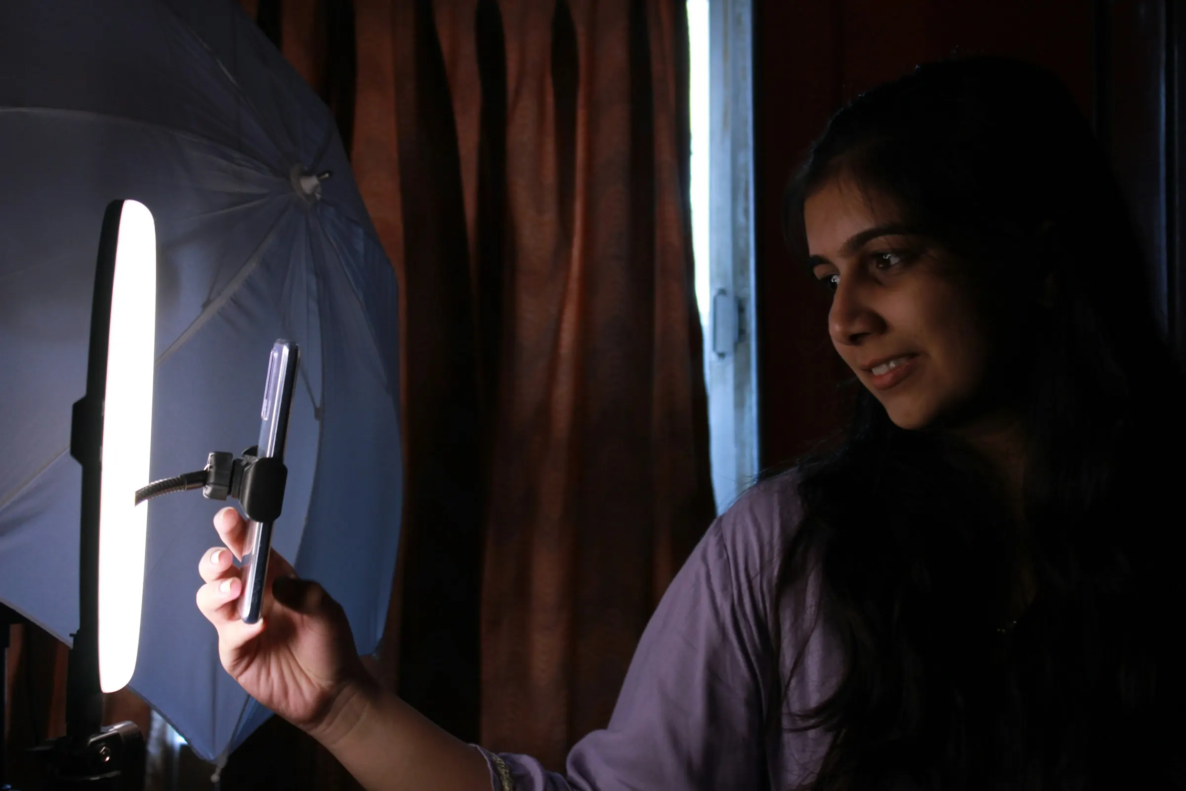 A creator filming herself on a phone under a soft light